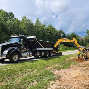 Dump truck hauling with an excavator and crew on a roadside job