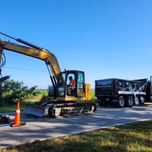Excavator digging a roadside ditch alongside a dump truck